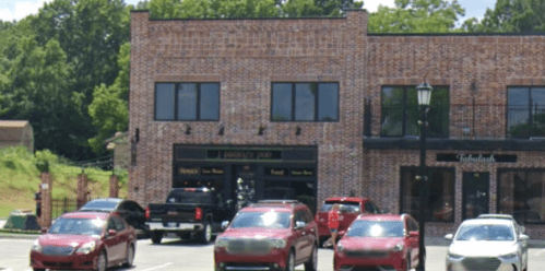 A brick building with a sign for "Patrick's Pub" and several parked cars in front. Trees are visible in the background.
