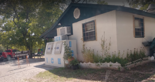A small building with an ice vending machine outside, surrounded by greenery and a sign that says "STOP PAY ATTENDANT."