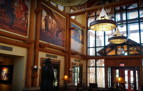 Interior of a lodge featuring large murals, wooden beams, and decorative lighting fixtures. Warm, inviting atmosphere.