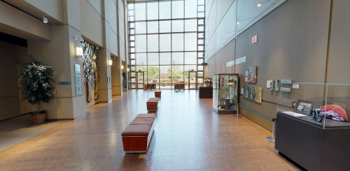 A spacious lobby with large windows, benches, and display cases featuring art and exhibits.