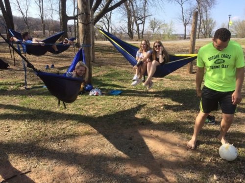 A group of friends relaxes in hammocks and on the grass, enjoying a sunny day outdoors near a soccer ball.