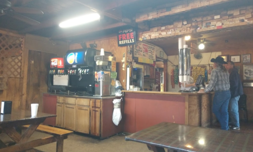 Interior of a rustic diner with a soda fountain, wooden tables, and two customers at the counter.