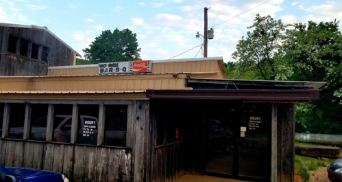 Exterior of a rustic barbecue restaurant with a sign reading "Wild Rose Bar-B-Q" and visible hours of operation.