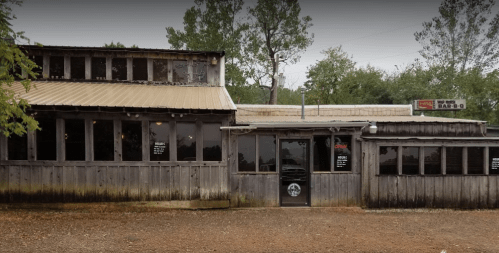A rustic wooden building with a metal roof, featuring large windows and a sign for a BBQ restaurant.