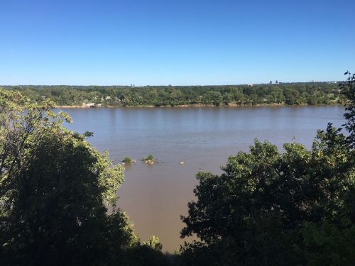 A serene river view surrounded by lush greenery under a clear blue sky.