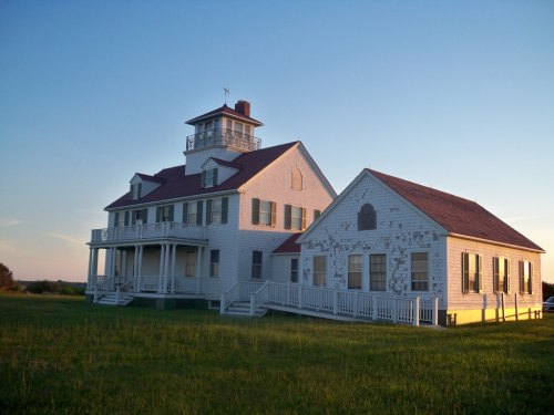 A large white house with a red roof, featuring a tower, surrounded by green grass under a clear blue sky.