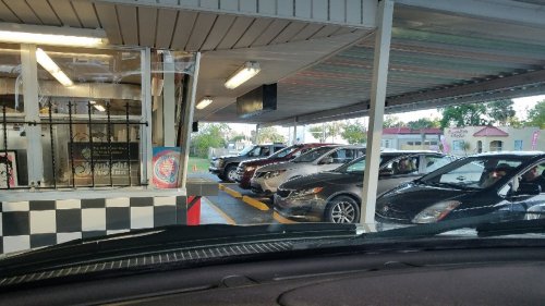 A view from a car in a drive-in with several vehicles lined up at a service window under a covered area.