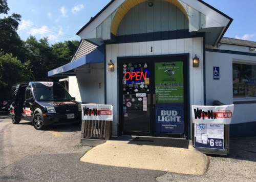 A small building with an "Open" sign, featuring advertisements and a parked vehicle outside.