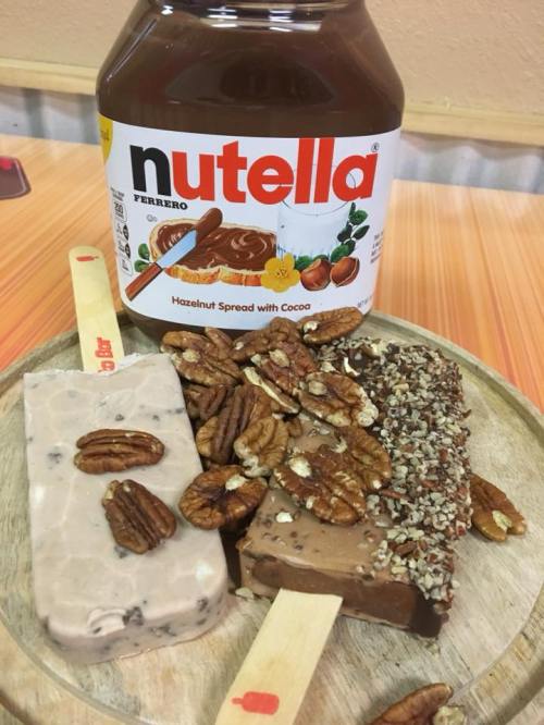 A wooden platter with two ice cream bars and pecans, alongside a jar of Nutella hazelnut spread.