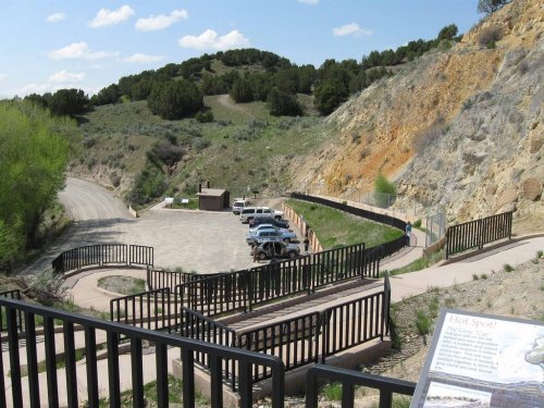 A scenic view of a parking area and pathway leading into a hilly landscape with greenery and a sign in the foreground.