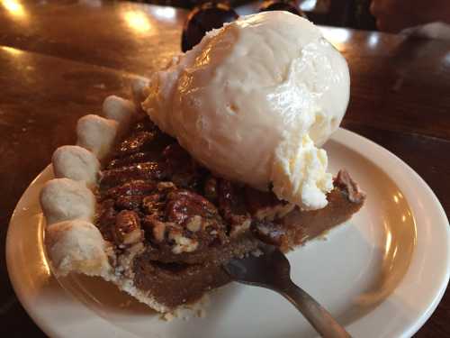 A slice of pecan pie topped with a scoop of vanilla ice cream on a white plate.