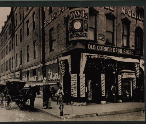 Historic street scene featuring a horse-drawn carriage and an old drug store with vintage signage.