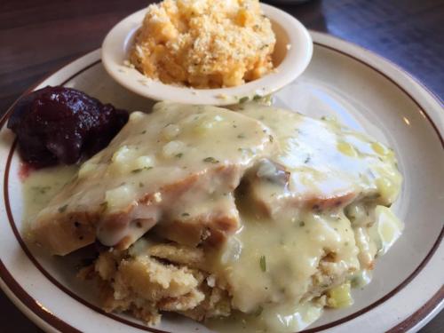 A plate of turkey with gravy over stuffing, served with a side of macaroni and cheese and cranberry sauce.