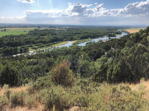 A scenic view of a river winding through lush green fields and trees under a partly cloudy sky.