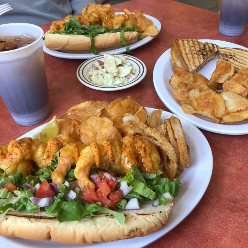 A table with shrimp sandwiches, potato chips, and a side of coleslaw, accompanied by iced tea in cups.