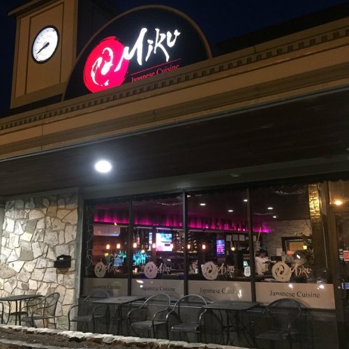 Exterior of Miku Japanese Cuisine restaurant at night, featuring a stone facade and illuminated signage.