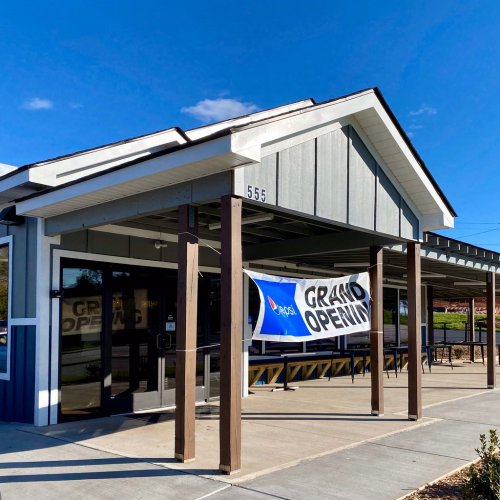 A building with a "Grand Opening" banner outside, featuring a modern design and clear blue sky.