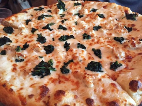 A close-up of a cheese pizza topped with green spinach leaves and golden-brown crust.