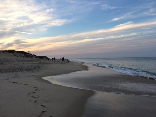 A serene beach at sunset, with gentle waves lapping the shore and people walking along the water's edge.