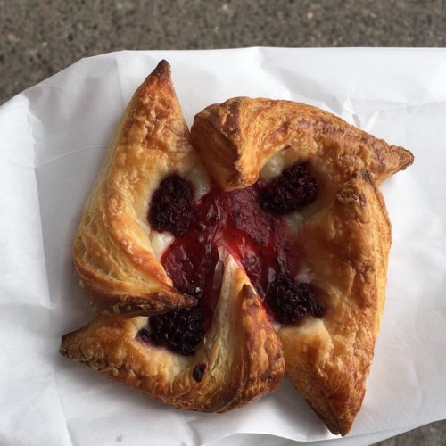A flaky pastry with a pinwheel shape, filled with red and black berry jam, resting on white paper.