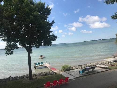 A serene lakeside view with a boat on the water, colorful chairs on the shore, and a clear blue sky.