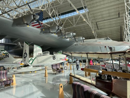 A spacious aircraft hangar featuring vintage planes and a large military aircraft in the background.