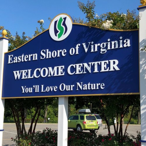 Sign for the Eastern Shore of Virginia Welcome Center, featuring a nature-themed design and a green vehicle in the background.