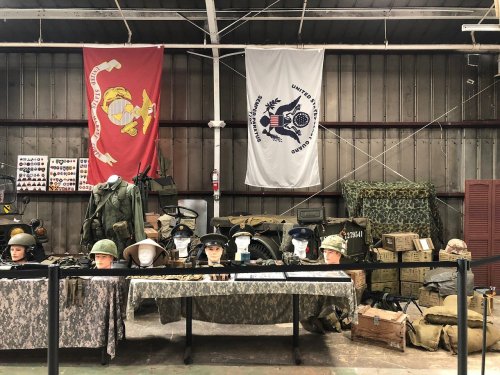 Display of military uniforms, helmets, and equipment with flags in a museum-like setting.