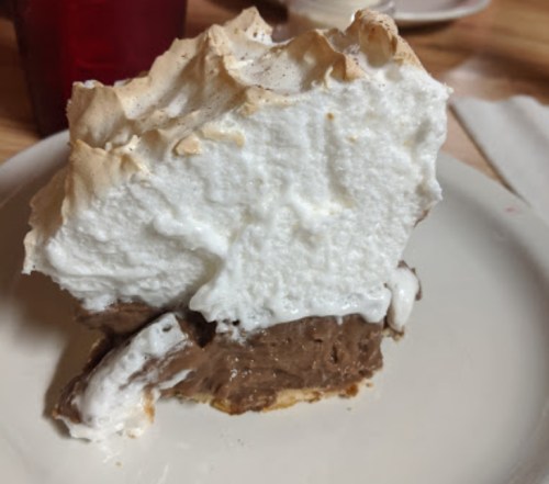 A slice of chocolate cream pie topped with fluffy meringue on a white plate.