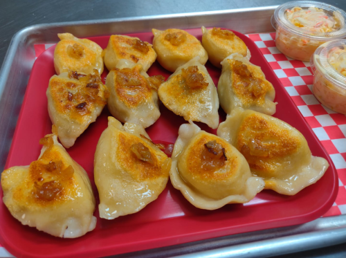 A tray of golden-brown dumplings, some with crispy edges, served alongside containers of coleslaw.