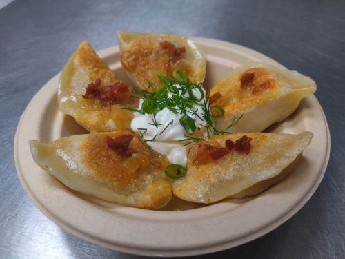 A plate of golden-brown dumplings garnished with herbs and served with a dollop of sour cream.