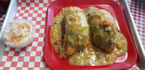 Two stuffed cabbage rolls covered in gravy, served on a red tray with a side of coleslaw in a plastic container.