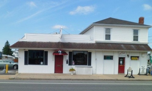 A white two-story building with a red door and awning, featuring a sign and windows, set against a blue sky.