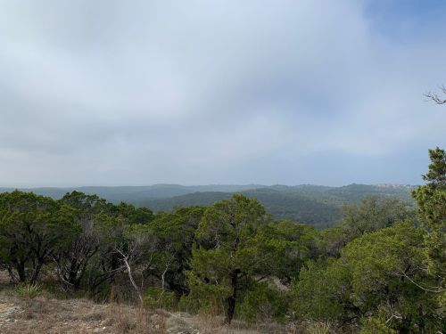 A scenic view of rolling hills and trees under a cloudy sky, showcasing a lush green landscape.