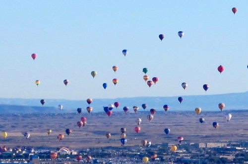 A sky filled with colorful hot air balloons floating over a landscape with distant mountains and a clear blue sky.