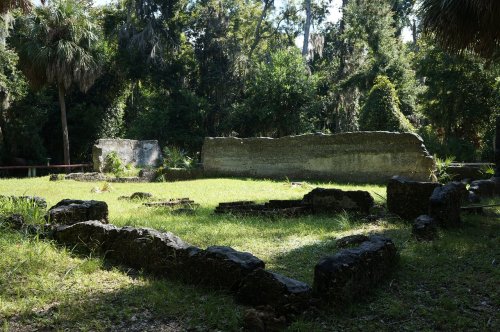 Ruins of stone structures surrounded by lush greenery in a forested area.
