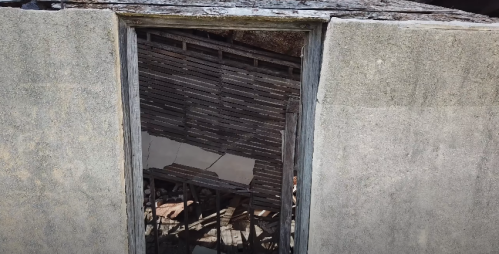 A view through a doorway of a dilapidated structure, revealing wooden beams and debris inside.