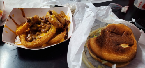 A plate of cheesy chili fries next to a slightly burnt burger in a takeout container.