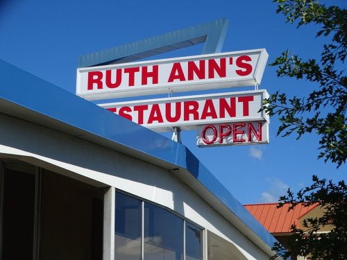 Sign for Ruth Ann's Restaurant with "OPEN" displayed, set against a clear blue sky.