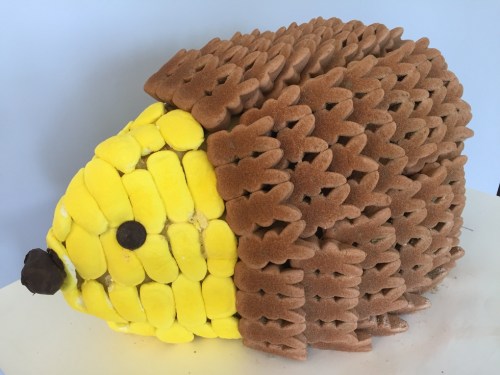 A cake shaped like a hedgehog, covered in brown and yellow sponge cake with a chocolate nose.