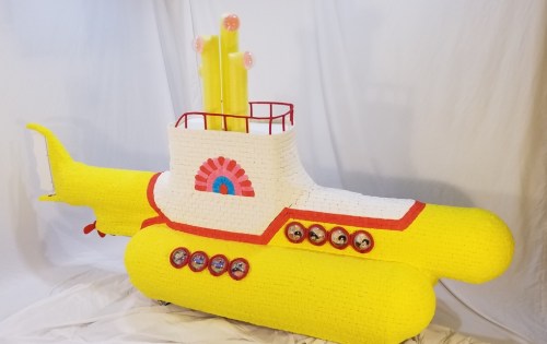 A bright yellow model submarine with colorful details and a whimsical design, set against a white background.