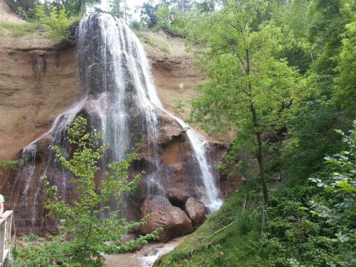 A serene waterfall cascading down a rocky cliff, surrounded by lush green trees and foliage.