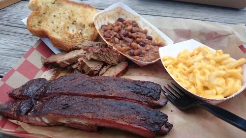 A plate featuring smoked brisket, baked beans, macaroni and cheese, and toasted bread.