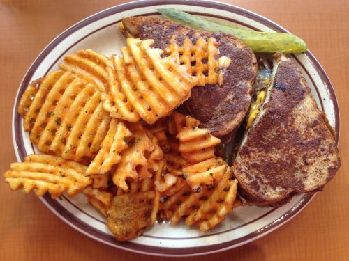 A plate of crispy waffle fries and a grilled sandwich with melted cheese, garnished with a pickle.