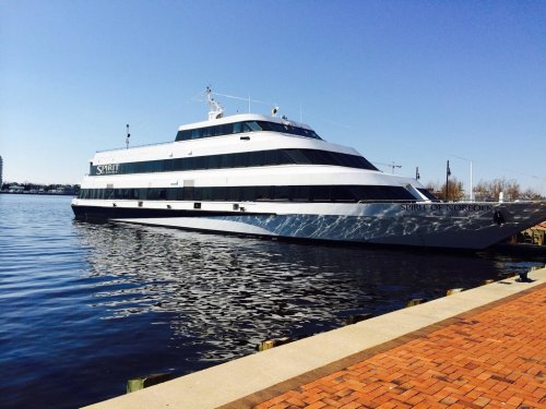 A large white yacht named "Spirit of Norfolk" docked by a waterfront on a clear, sunny day.