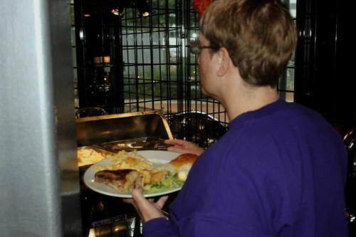 A person in a purple shirt holds a plate of food while looking into a serving area.