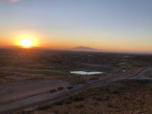 Sunset over a vast landscape, with mountains in the distance and a small pond reflecting the warm colors of the sky.