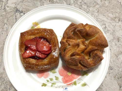 A plate with two pastries: one with strawberries and glaze, the other twisted and golden brown.