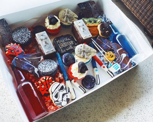 A box of Star Wars-themed treats, including cupcakes, cookies, and drinks, featuring characters and iconic symbols.