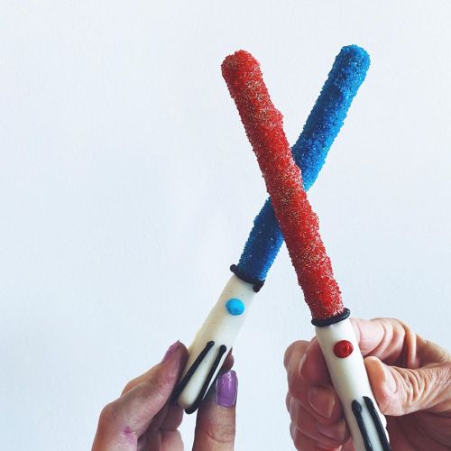 Two colorful candy sticks, one red and one blue, crossed like lightsabers against a white background.